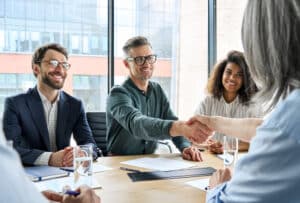 Happy,Businessman,And,Businesswoman,Shaking,Hands,At,Group,Board,Meeting.